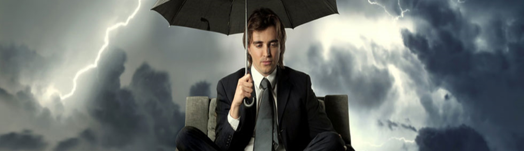 sad man sitting in chair with umbrella covering him